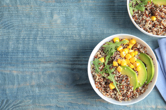 Healthy quinoa salad with vegetables in bowls on wooden table, top view. Space for text