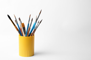 Holder with different paint brushes on white background. Space for text