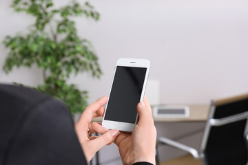 Woman holding mobile phone with blank screen in office, closeup. Space for text
