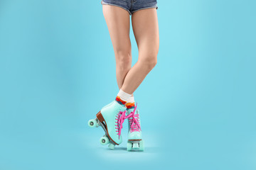 Young woman with retro roller skates on color background, closeup