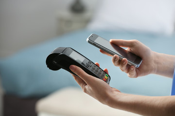 Woman using modern payment terminal with mobile phone indoors, closeup