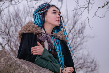 Pensive girl with blue hair dreadlocks in the woods on the rocks. Woman viking dreams and looks...