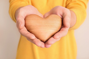 Man holding wooden heart in hands on color background, closeup