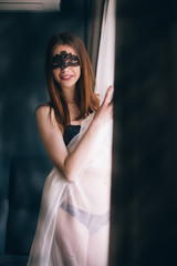 Fototapeta na wymiar Beautiful caucasian girl drssed in black lingerie with a sensual mask wrapped herself with a tent , natural light.