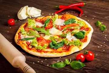 Pizza Italian with mozzarella, parmezan cheese, red tomatoes and fresh green basil, arugula and cabbage leaves on a brown table decorated by mozzarella, red sweet pepper, cherry and battledore