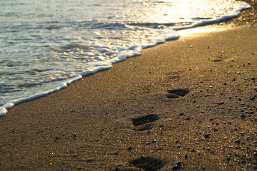 Fototapeta na wymiar Vanishing feet traces washing off by waves from golden beach sand with reflection of setting sun in receding water