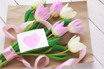women's Day. a bouquet of tulips on a white wooden background with a card with hearts. selective focus