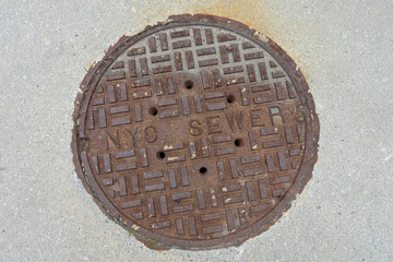 Old rusty sewer hatch on concrete surface, New York City.