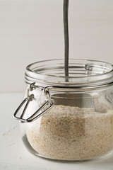 Heap of psyllium husk also called isabgol in glass jar with metal spoon on white table background