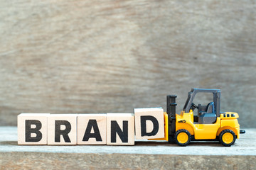 Toy forklift hold letter block d to complete word brand on wood background