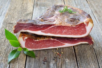 Südtiroler Speck am Stück: Eine Hamme in zwei Hälften geteilt auf einem Holztisch – Typical...