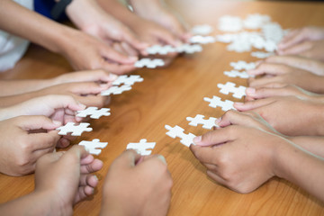 Hands of diverse people assembling jigsaw puzzle, team put pieces together searching for right match, help support in teamwork to find common solution concept, top close up view