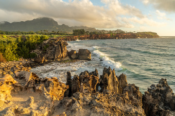 Pacific ocean waves crashing against the lithified sand dunes making up the makawehi Bluff, Haupu Mountain in the background, Poipu, Koloa, Kauai, Hawaii