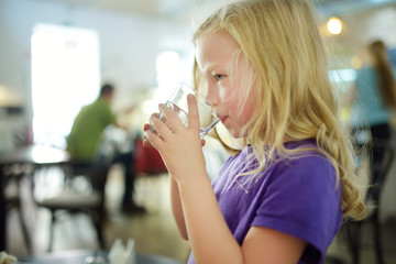 Cute little girl drinking water on hot summer day.