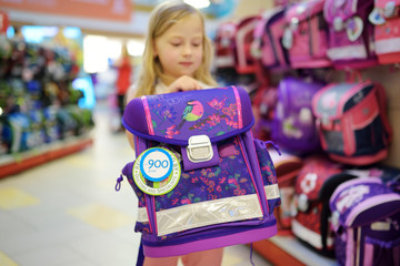 Cute little girl choosing a schoolbag before starting classes. Adorable pupil buying school backpack in a store. - obrazy, fototapety, plakaty