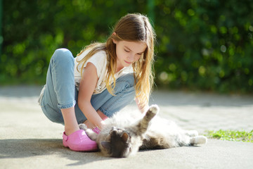 Cute young girl with her cat on sunny autumn day. Adorable child petting her kitty.