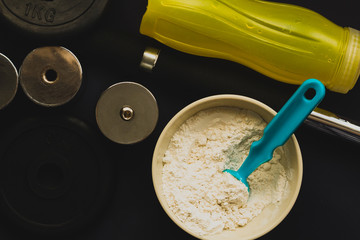 Tazón de Proteína en polvo sabor vainilla junto a Pesas, mancuernas y artículos de gimnasio - nutrición y ejercicio  -  estilo de vida saludable