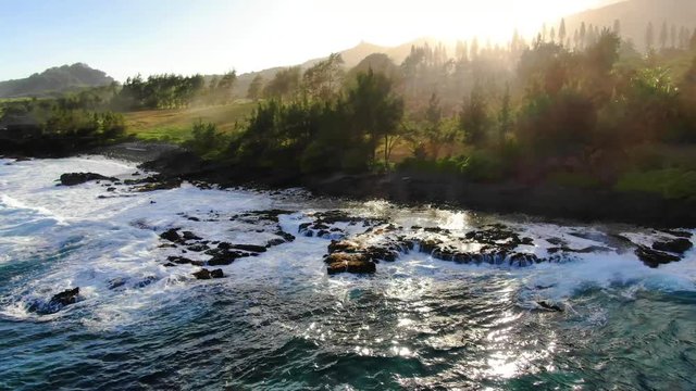Stunning aerial drone sunset footage of the coastal area near the town of Hana on the east side of the island of Maui, Hawaii. Spray in the air, Haleakala volcano National Park in the background.