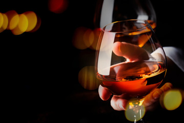 French glowing cognac glass in hand on the dark bar counter background, copy space, selective focus