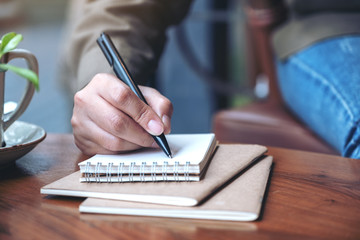 Fototapeta premium Closeup image of a woman's hand writing on blank notebook with coffee cup on wooden table