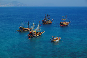 Fototapeta na wymiar Tourist sail boats in turquoise waters of the Mediterranean sea beside the Turkish ancient fortress Alanya. Antalya, Turkey.