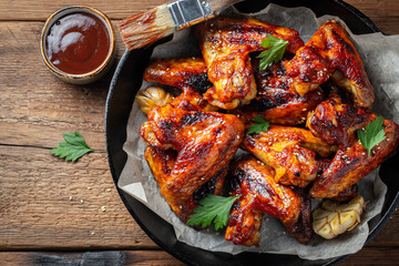 Baked chicken wings in barbecue sauce in a cast iron pan on an old wooden rustic table. Top view