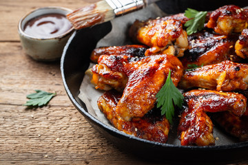 Baked chicken wings in barbecue sauce in a cast iron pan on an old wooden rustic table