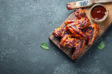 Roasted chicken wings in barbecue sauce with sesame seeds and parsley on a wooden board on a...