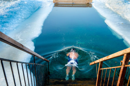 A woman from the back dived into the icy water. Extreme water sport. Ice hole swimming. Winter vacation. Winter, very cold, blue water, ice around the edges.