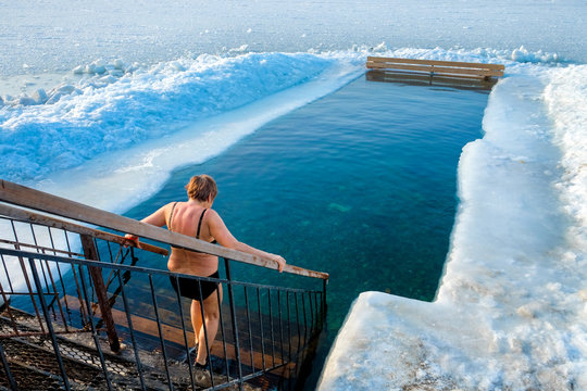 A Woman From The Back, Goes To The Ice Hole. Extreme Water Sport. Ice Hole Swimming. Winter Vacation. Winter, Very Cold, Blue Water, Ice Around The Edges.