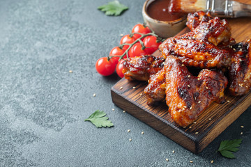 Roasted chicken wings in barbecue sauce with sesame seeds and parsley on a wooden board on a concrete table. With copy space. Tasty snack for beer on a dark background