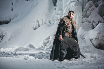 Man dressed in medieval armor and raincoats with swords in winter at the mountains under snow...