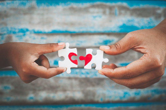 Parent and kid hands connecting couple jigsaw puzzle piece with drawn red heart