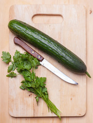 cucumber and parsley on wooden cutting board with knife, top view