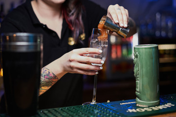The female barman creates hard alcoholic shots at the bar at the restaurant. The barman pours alcohol into shots.