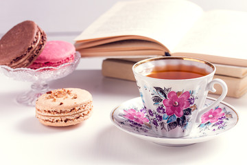 A cup of black tea with macaroons and books on a white wooden background.