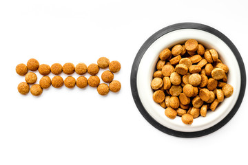 Dog food. Dry food in shape of bone near bowl on white backgorund top view space for text