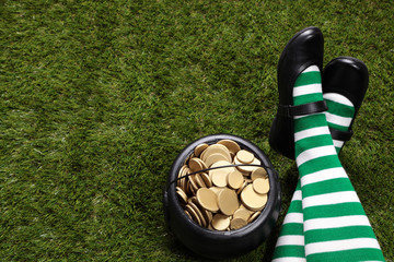 Girl with Leprechaun's striped socks sitting on grass next to a black cauldron full of golden coins
