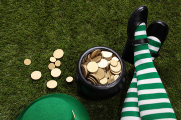 Girl wearing Leprechaun's striped socks sitting on grass next to a black cauldron full of golden...