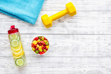 Healthy lifestyle, healthy habits. Detox water, fruit salad, sport equipment dumbbells on white wooden background top view copy space