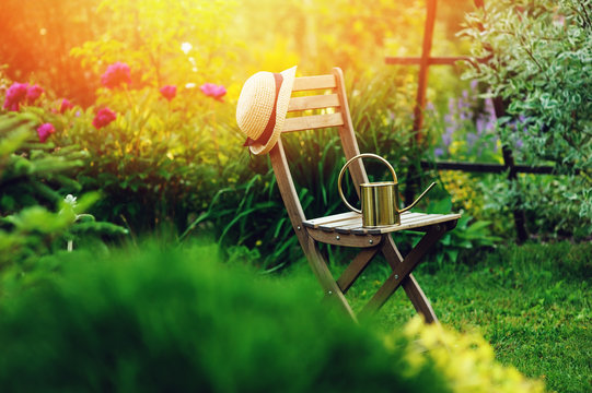 beautiful blooming summer private garden with wooden chair, gardener hat and watering can