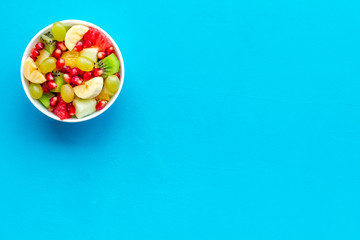 Light healthy breakfast or appetizer. Fruit salad with apple, kiwi and pomegranate in bowl on blue background top view space for text