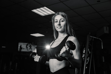 Fototapeta na wymiar Young and beautiful woman working out with dumbbells in gym. Biceps curls.
