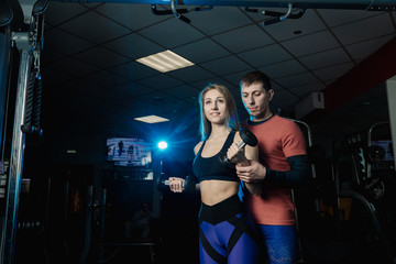 Fototapeta na wymiar Active beautiful fitness model girl trains biceps with dumbbells together with a trainer in the gym.