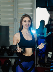 Young and beautiful woman working out with dumbbells in gym. Biceps curls.