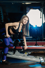 Fototapeta na wymiar Side view of beautiful fitness woman workout with weights over exercise bench at gym.