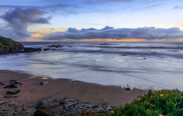 Pastel colors of sunset and silky water from long exposure of waves crashing by Pigeon Point Lighthouse on Northern California Pacific Ocean coastline at sunset