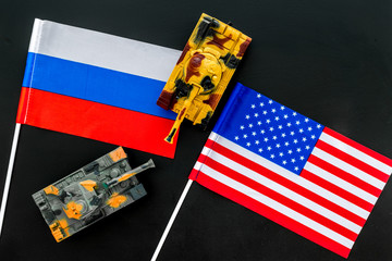 War, confrontation concept. Russia, USA. Tanks toy near russian and american flag on black background top view