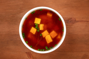 An overhead photo of a bowl of miso soup with tofu and scallions on a dark rustic background with a place for text