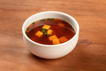 A photo of a bowl of miso soup with tofu and scallions on a dark rustic background with copy space